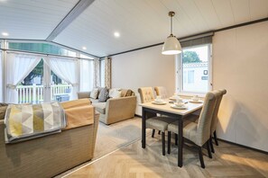 Una sala moderna con sofá, una mesa de comedor con sillas y un ventanal con cortinas.