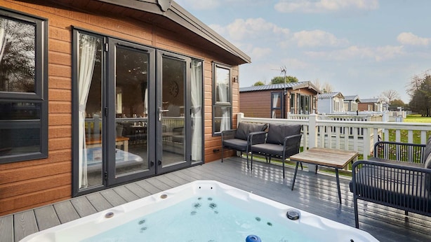 A wooden deck with a hot tub, outdoor furniture, and sliding glass doors leading to a patio area. - Host Stay Fairview Lodge (York)