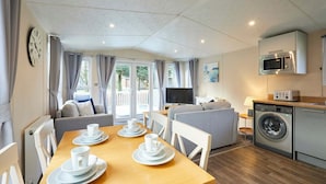 A modern kitchen with a microwave, oven, and washing machine. There is a dining area with a table set for two, and a living area with a sofa and TV. - Host Stay Fairview Lodge (York)