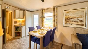 A cozy dining area with a table set for four, a clock on the wall, and a framed painting above the table. - Host Stay The Major Oak Lodge (York)