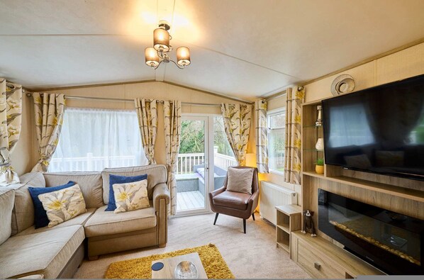 A cozy living room with a sofa, armchair, and TV. There is a glass door leading to an outdoor area. - Host Stay The Major Oak Lodge (York)