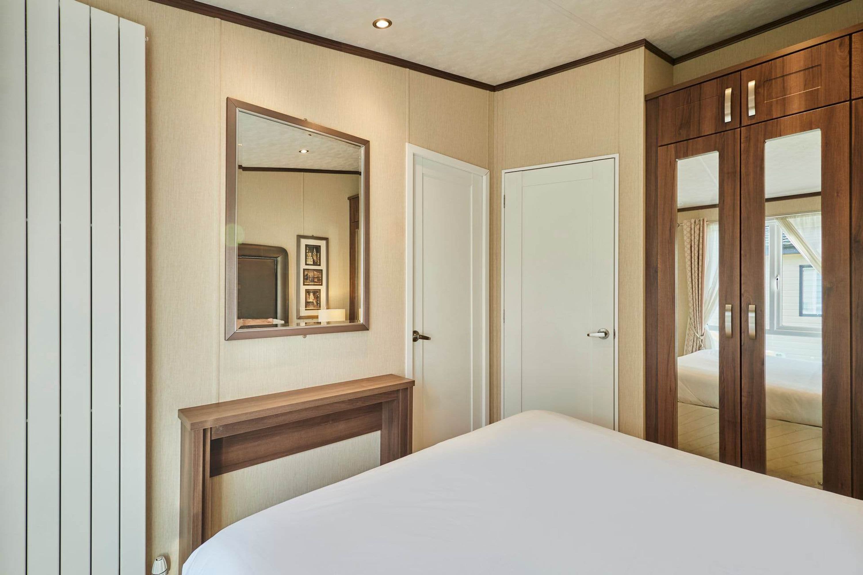 Een slaapkamer met een bed, een houten hoofdbord, een spiegel, een kledingkast en een deur.