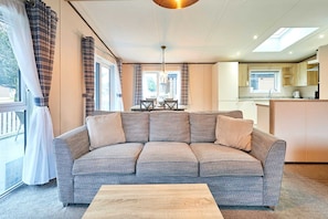 A modern living room with a grey sofa, a wooden coffee table, and a dining area with a table and chairs. - Host Stay Truemans Lodge (York)