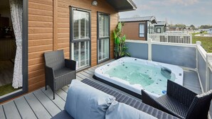 Eine Holzterrasse mit Whirlpool, Sitzgelegenheiten im Freien und Blick auf andere Hütten.