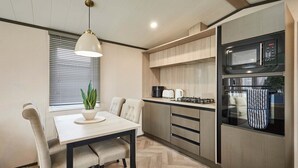 A modern kitchen with a dining table, chairs, a hanging light fixture, a microwave, an oven, and a coffee maker. - Host Stay The Kestrel Lodge (York)