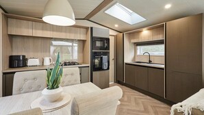 A compact kitchen with a microwave, oven, and sink, a dining area with a table and chairs, and a ceiling skylight. - Host Stay The Kestrel Lodge (York)