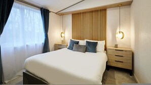 Een moderne slaapkamer met een groot bed, twee nachtkastjes, een houten hoofdbord en twee wandlampen.