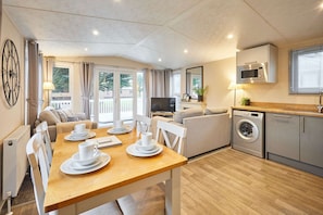 A modern kitchen with a microwave, washing machine, and a dining area with a table set for four. - Host Stay Woodpark Lodge (York)