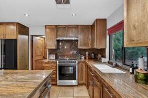 Une cuisine moderne avec des meubles en bois, une cuisinière en acier inoxydable et une grande fenêtre donnant sur un paysage verdoyant.