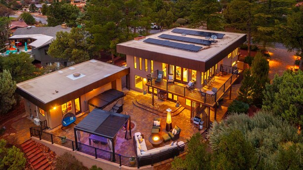 Een modern huis met een plat dak, zonnepanelen en een ruime terras met zitplaatsen en een vuurkorf.