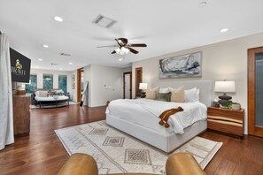 Une chambre spacieuse avec un grand lit, un ventilateur de plafond et une vue sur le salon.