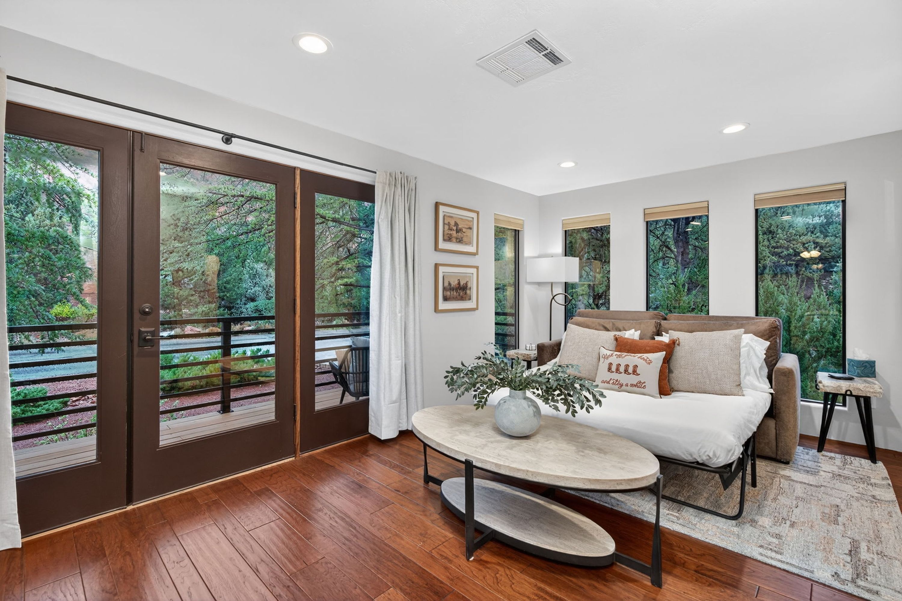 A modern living room with a sofa, a coffee table, and a view of a garden through large sliding glass doors.