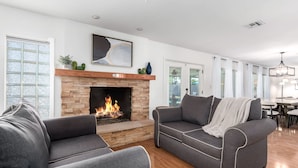 A modern living room with a fireplace, two grey sofas, and a dining area in the background. - NEW - The Desert Bloomhouse With Heated Pool (Scottsdale)