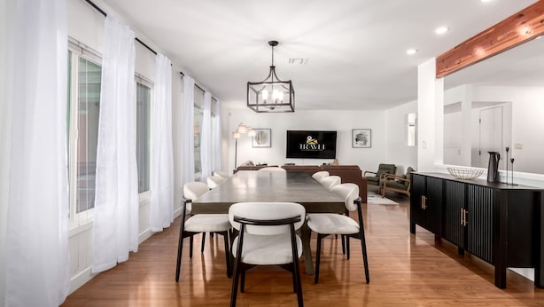 A modern dining area with a long table and chairs, a black cabinet with gold handles, and a TV on the wall. - NEW - The Desert Bloomhouse With Heated Pool (Scottsdale)