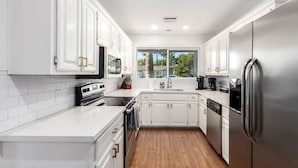 A modern kitchen with white cabinetry, stainless steel appliances, and a wooden floor. - NEW - The Desert Bloomhouse With Heated Pool (Scottsdale)