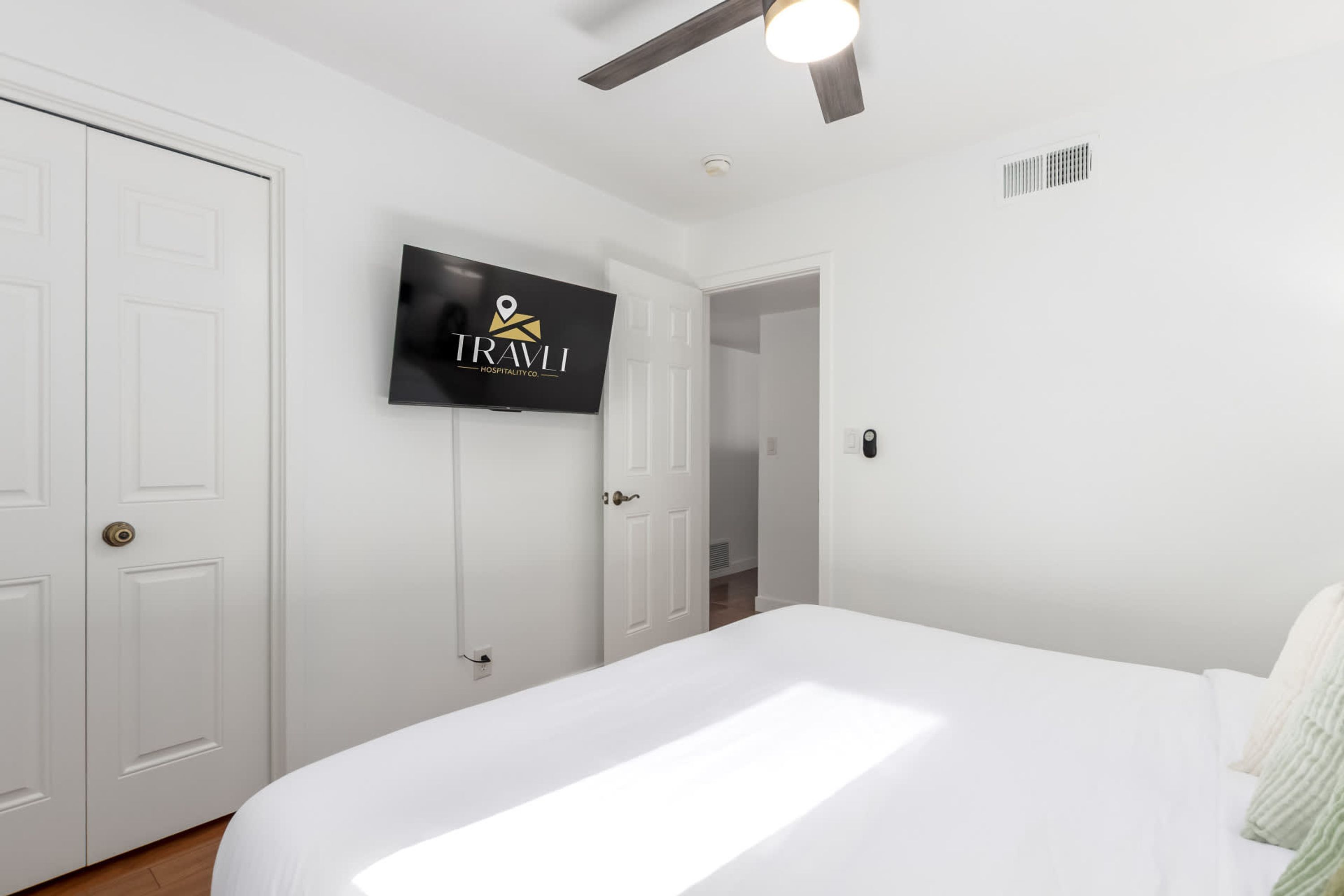 A hotel room with a bed, a TV mounted on the wall, and a ceiling fan.