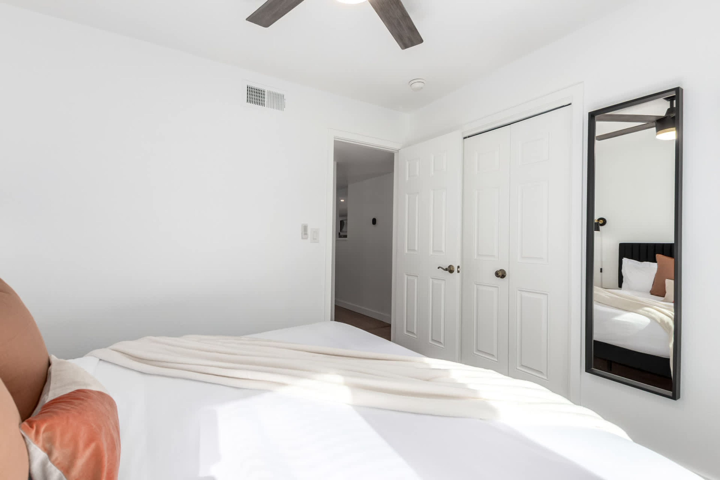 Une chambre à coucher comprenant un lit, une armoire, un miroir et un ventilateur de plafond.