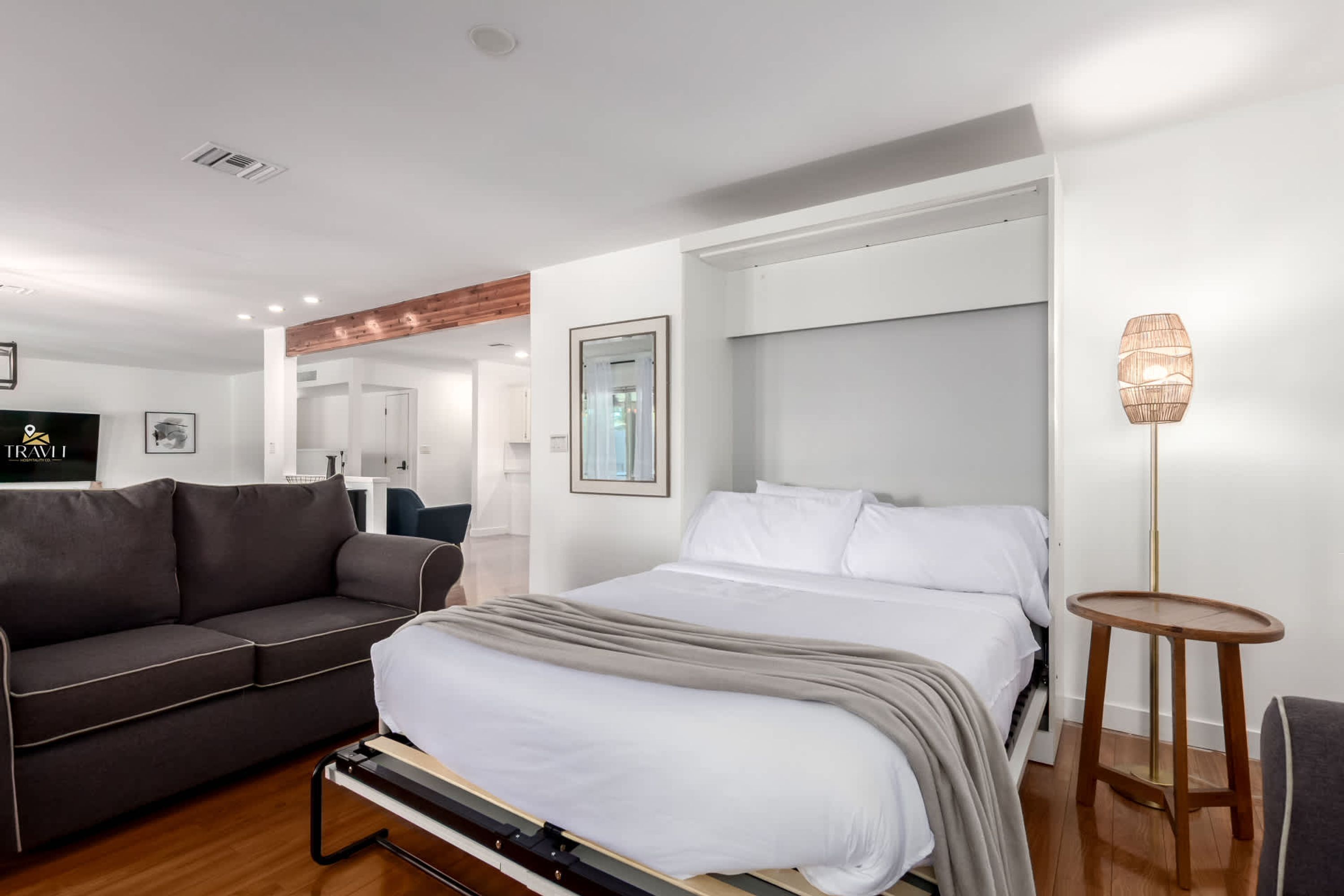 Ein modernes Hotelzimmer mit einem Bett, einer Couch, einem kleinen Tisch und einem an der Wand befestigten Fernseher.