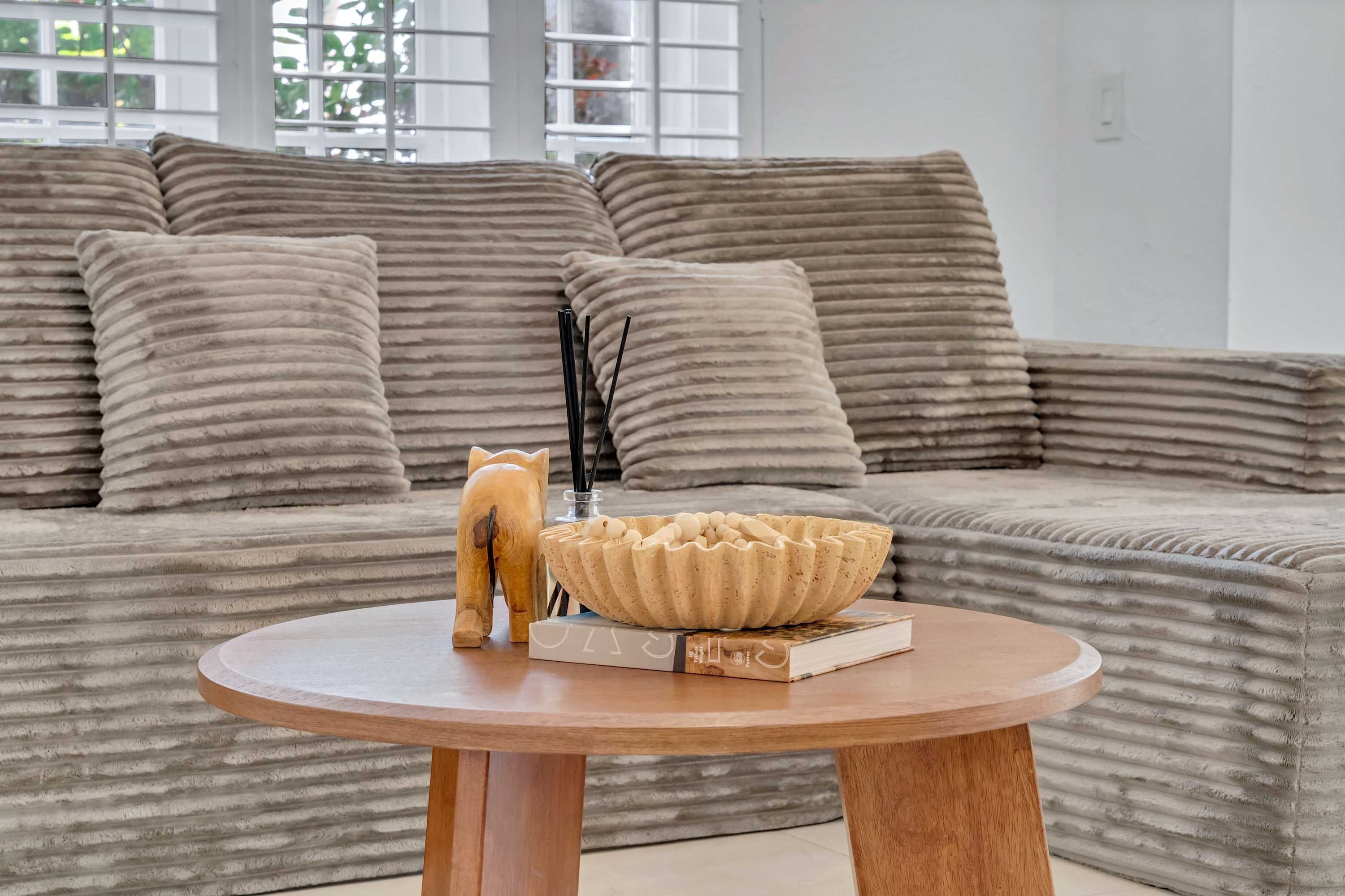 En moderne stue med en beige sofa, et rundt træbord og en dekorativ træfigur af en hest.