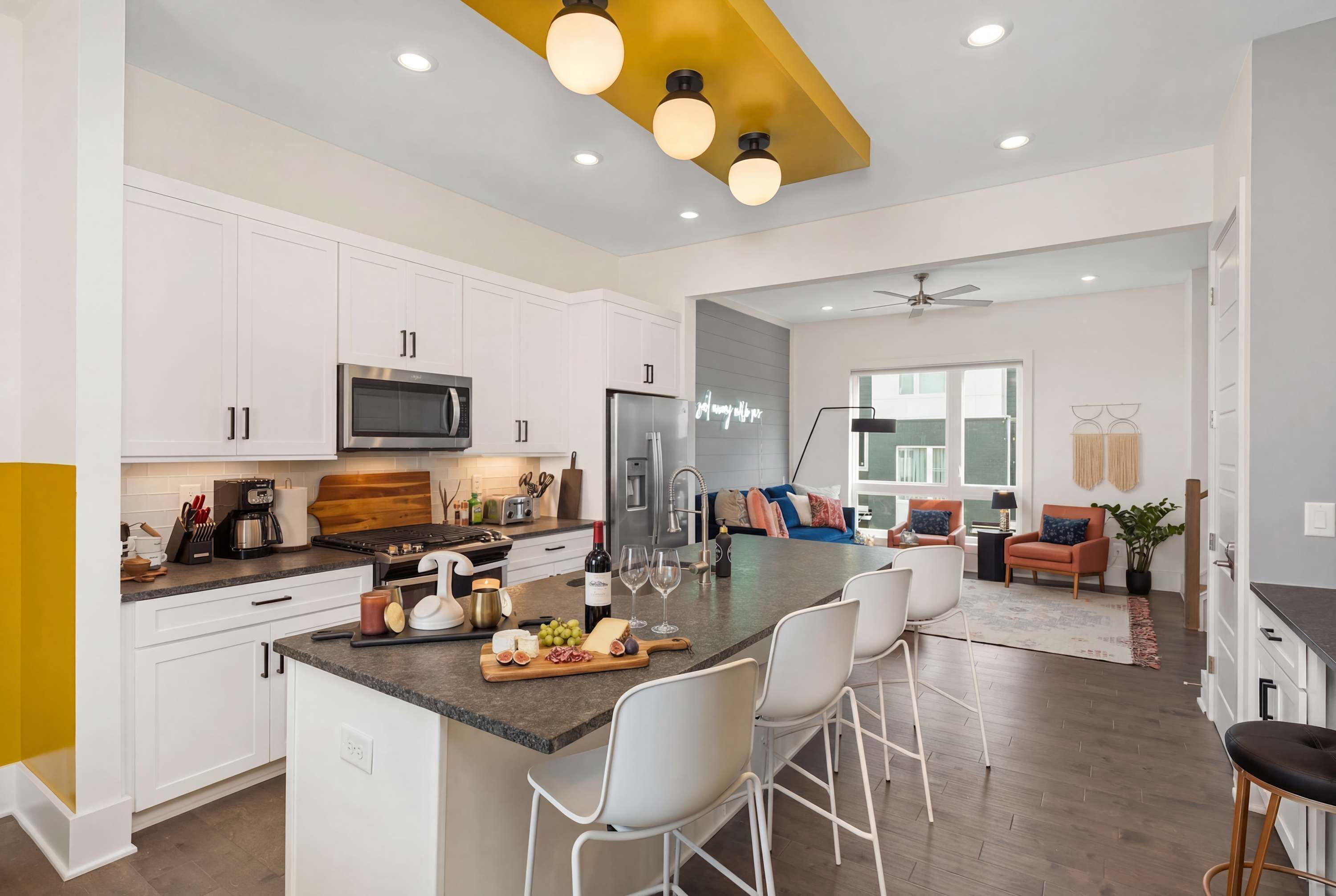 A modern kitchen with white cabinets, a central island with bar stools, and a dining area with a sofa and chairs.