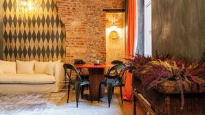 Un accogliente soggiorno con parete in mattoni, un arazzo decorativo, un tavolo rotondo in legno con sedie, un divano e una pianta ornamentale.