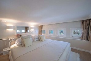 A large bed with a white comforter and pillows, a bedside table with a lamp, and a window with curtains. - Luxury Historic Villa, Heated Jacuzzi, Lemon Garden & Stunning Amalfi Sea Views (Amalfi)