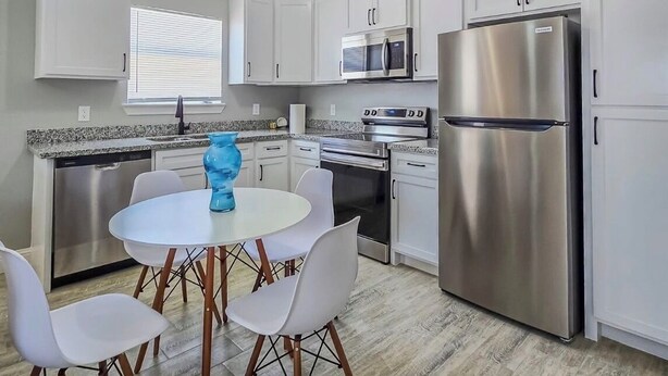 Una cocina moderna con gabinetes blancos, electrodomésticos de acero inoxidable y una mesa de comedor redonda con sillas.
