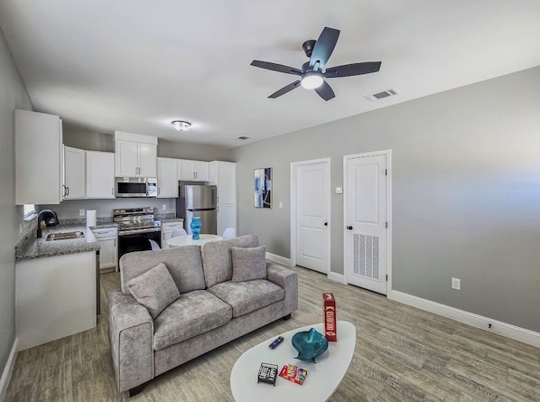 A compact living space with a kitchenette, a grey sofa, and a ceiling fan.