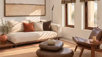 A living room with a sofa, a round wooden coffee table, a leather armchair, and a small side table with a candle.