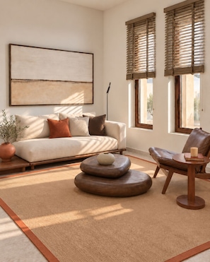 A living room with a sofa, a round wooden coffee table, a leather armchair, and a small side table with a candle. - Agali Hotel Milos (Milos)