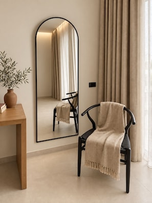 A room with a wooden table, a chair with a beige throw, a large mirror, and a window with curtains. - Agali Hotel Milos (Milos)
