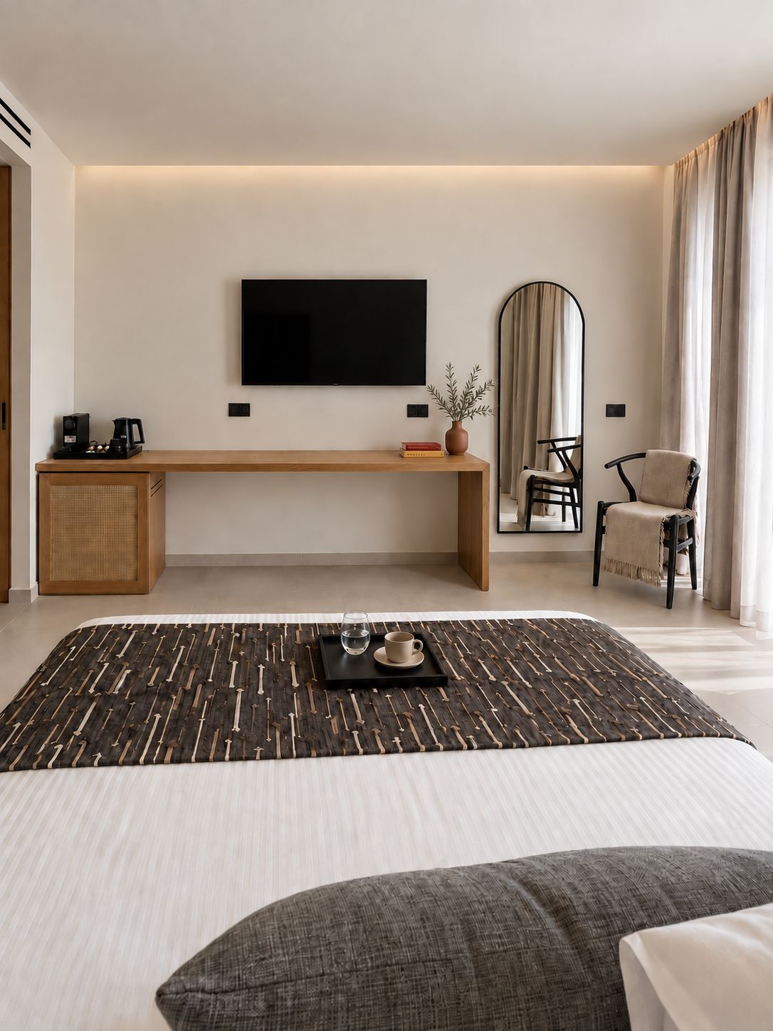Una moderna camera d'albergo con un letto grande, una TV a schermo piatto fissata al muro, una panca in legno, una sedia e un comodino con una macchina per il caffè.