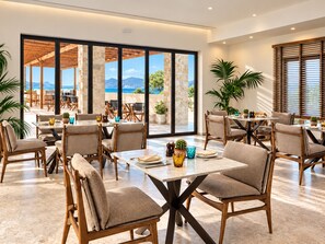 A spacious dining area with high ceilings and large windows offering a view of the outdoors. - Agali Hotel Milos (Milos)