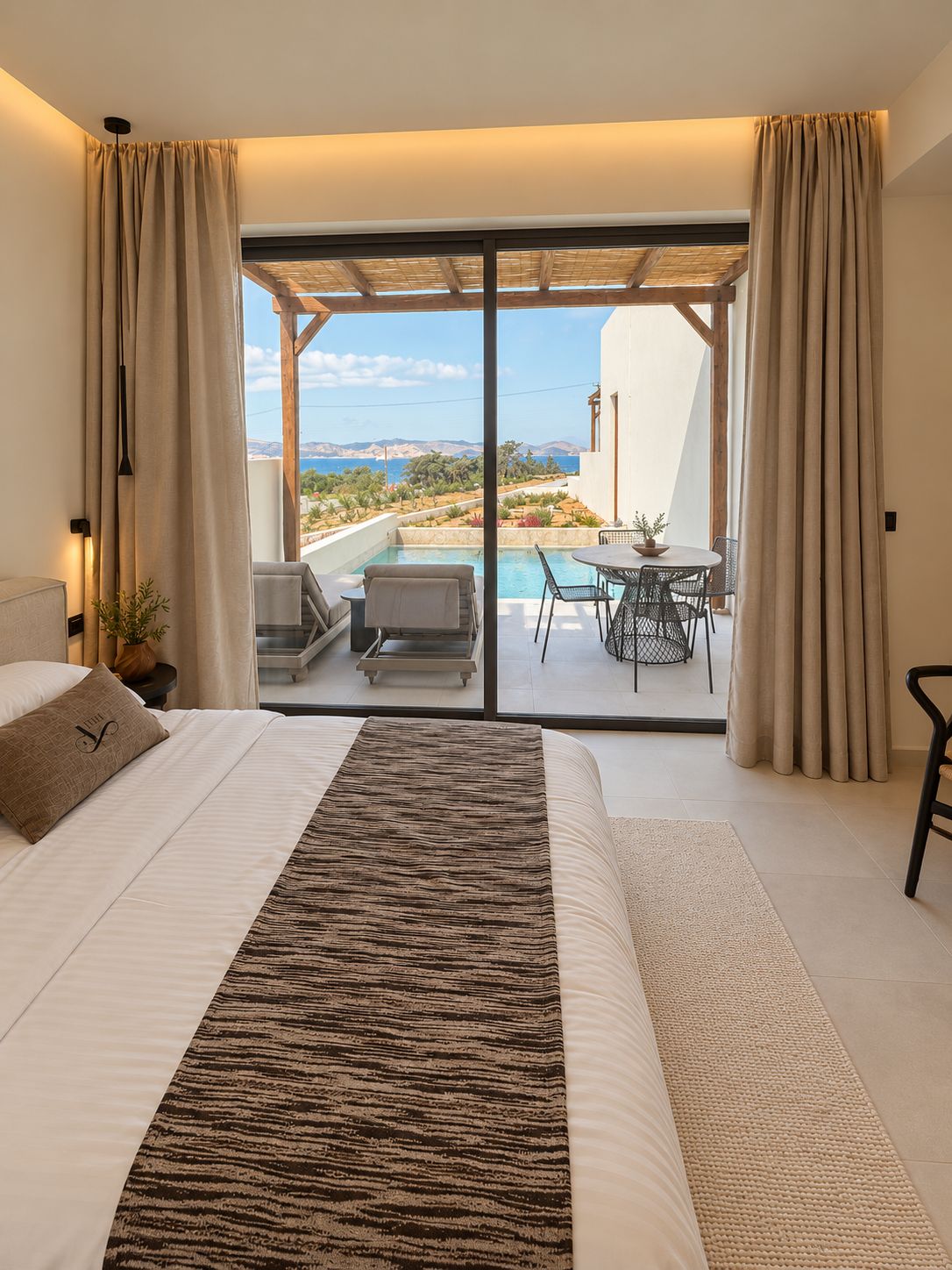 Un dormitorio con una cama grande, vistas a una piscina y zona de estar exterior, y un balcón con cortinas.