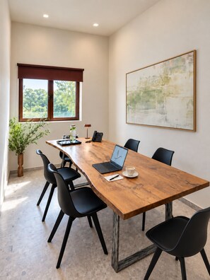 A conference room with a long wooden table, black chairs, a laptop, a coffee cup, and a potted plant. - Agali Hotel Milos (Milos)
