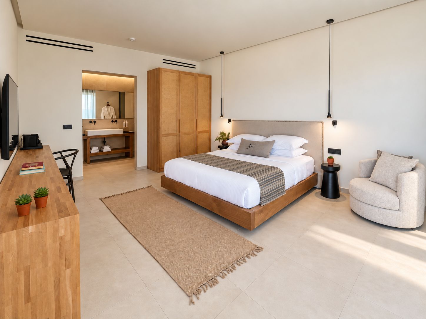 A modern bedroom with a wooden bed, a sitting area with a chair, and a bathroom visible through an open door.
