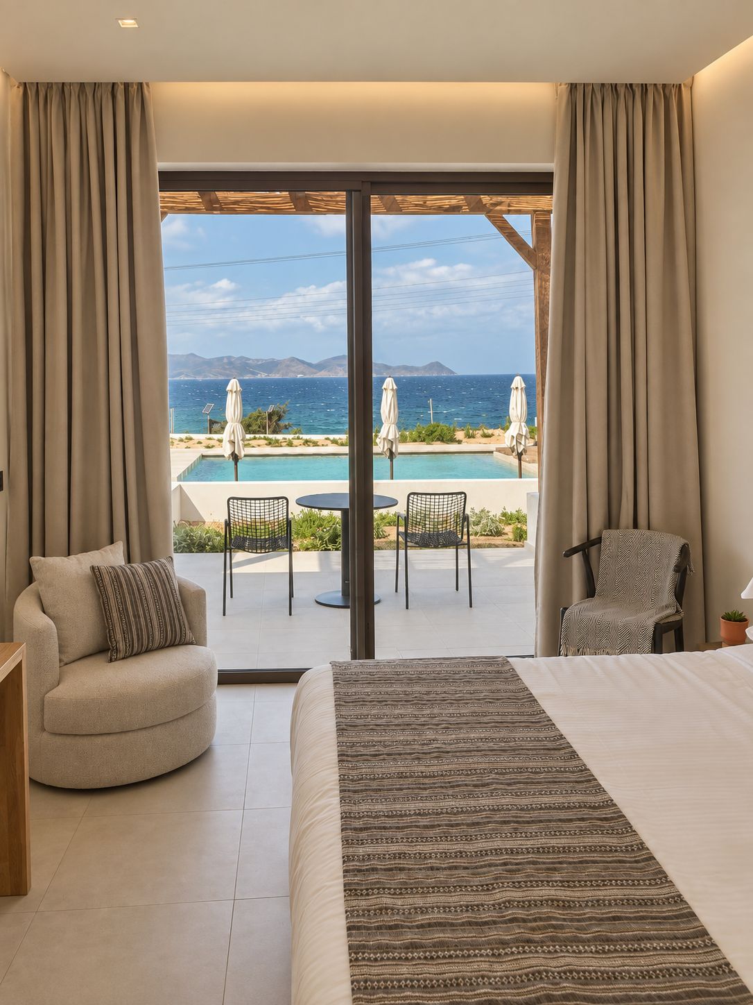 Habitación de hotel con una cama grande, vistas al mar, piscina y zona de estar exterior.