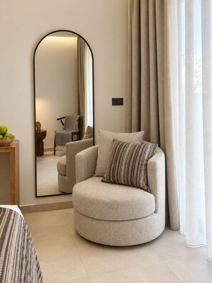 A modern living room with a round armchair, a large mirror, and a view through sheer curtains. - Agali Hotel Milos (Milos)