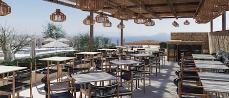 An outdoor dining area with multiple tables and chairs, a thatched roof, and hanging wicker lamps.