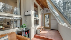 Un interior moderno con una escalera que sube a un altillo, ventanas amplias y una zona de estar acogedora con un sofá y una mesita.