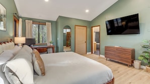 Un dormitorio con una cama grande, un televisor montado en la pared, un tocador y una ventana con cortinas.