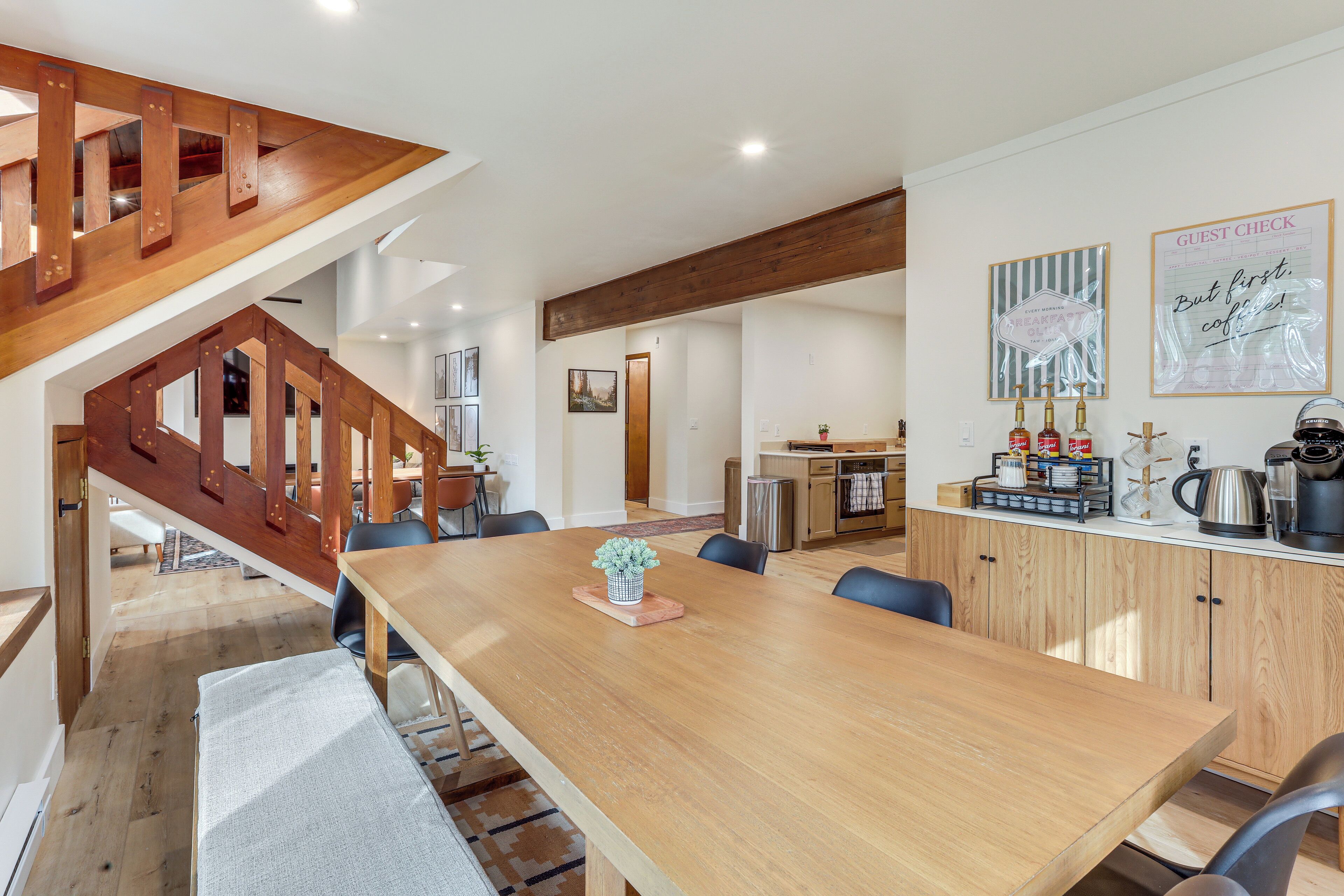A spacious dining area with a wooden table and chairs, a kitchen area with wooden cabinets, and a staircase with wooden railings.