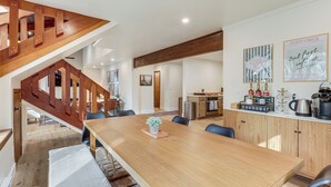 Un comedor espacioso con una mesa y sillas de madera, un área de cocina con armarios de madera y una escalera con barandillas de madera.