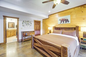 A bedroom with a wooden bed frame, a ceiling fan, a wooden wall panel, and a bear painting. - Game Room + Deck: Spacious Spruce Pine Retreat! (Spruce Pine)