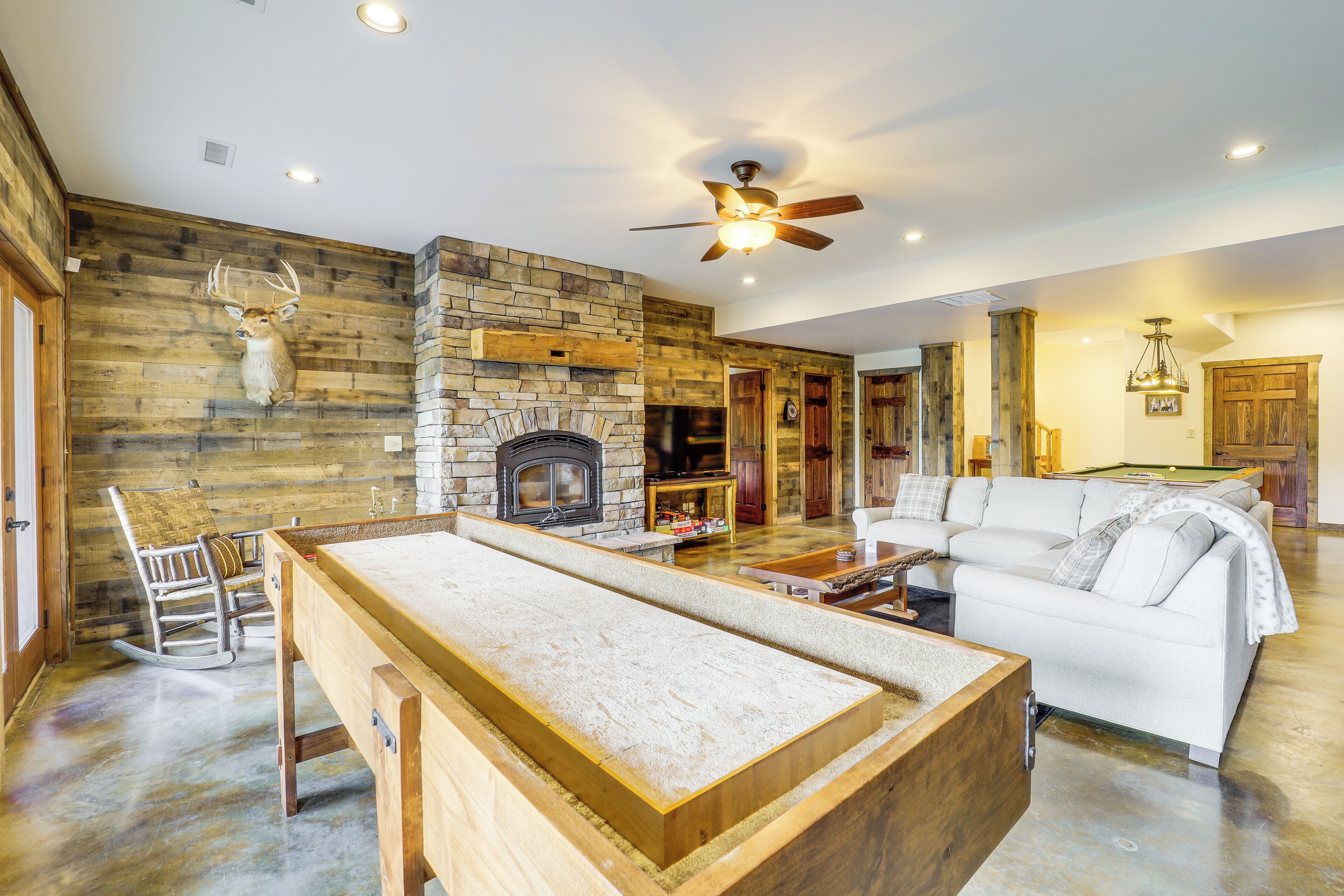 A spacious living room with a pool table, a stone fireplace, and a white sofa.