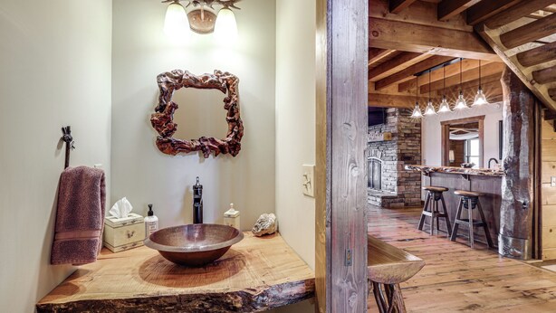 Une salle de bain rustique avec un lavabo en bois, un grand miroir et un mur en pierre.