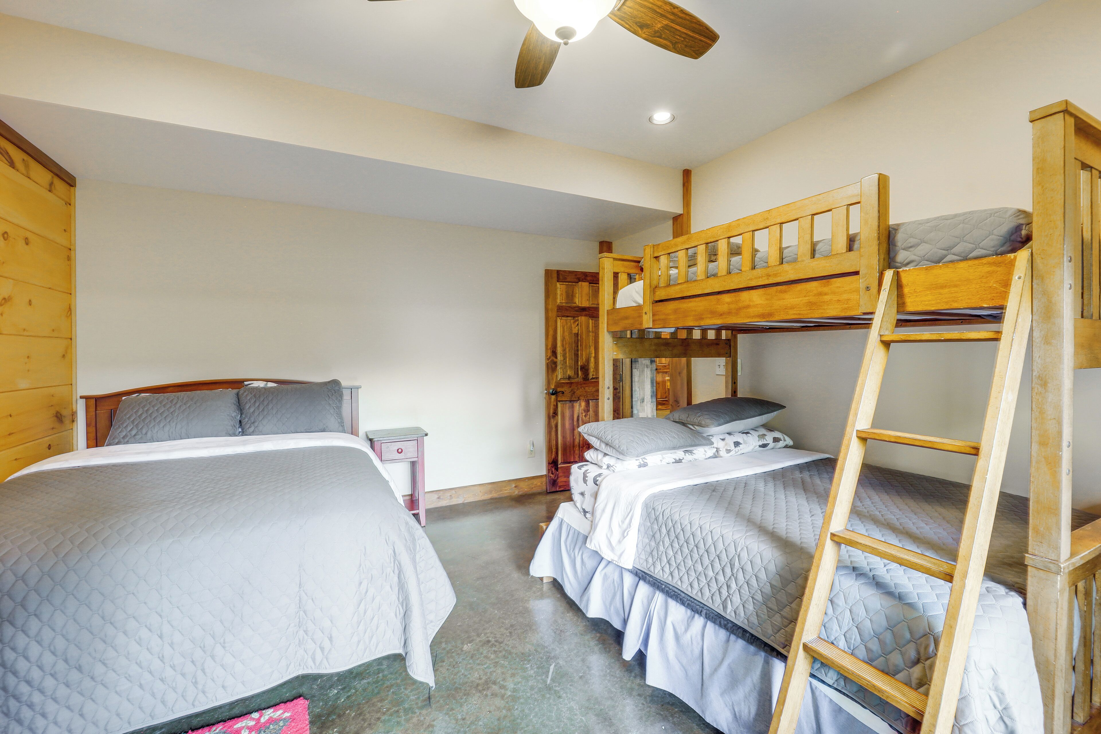 A room with bunk beds, a wooden ladder, a nightstand, and a ceiling fan.
