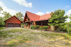 A two-story log cabin with a red metal roof, a separate garage, and a well-maintained front yard with gravel and greenery. - Game Room + Deck: Spacious Spruce Pine Retreat! (Spruce Pine)