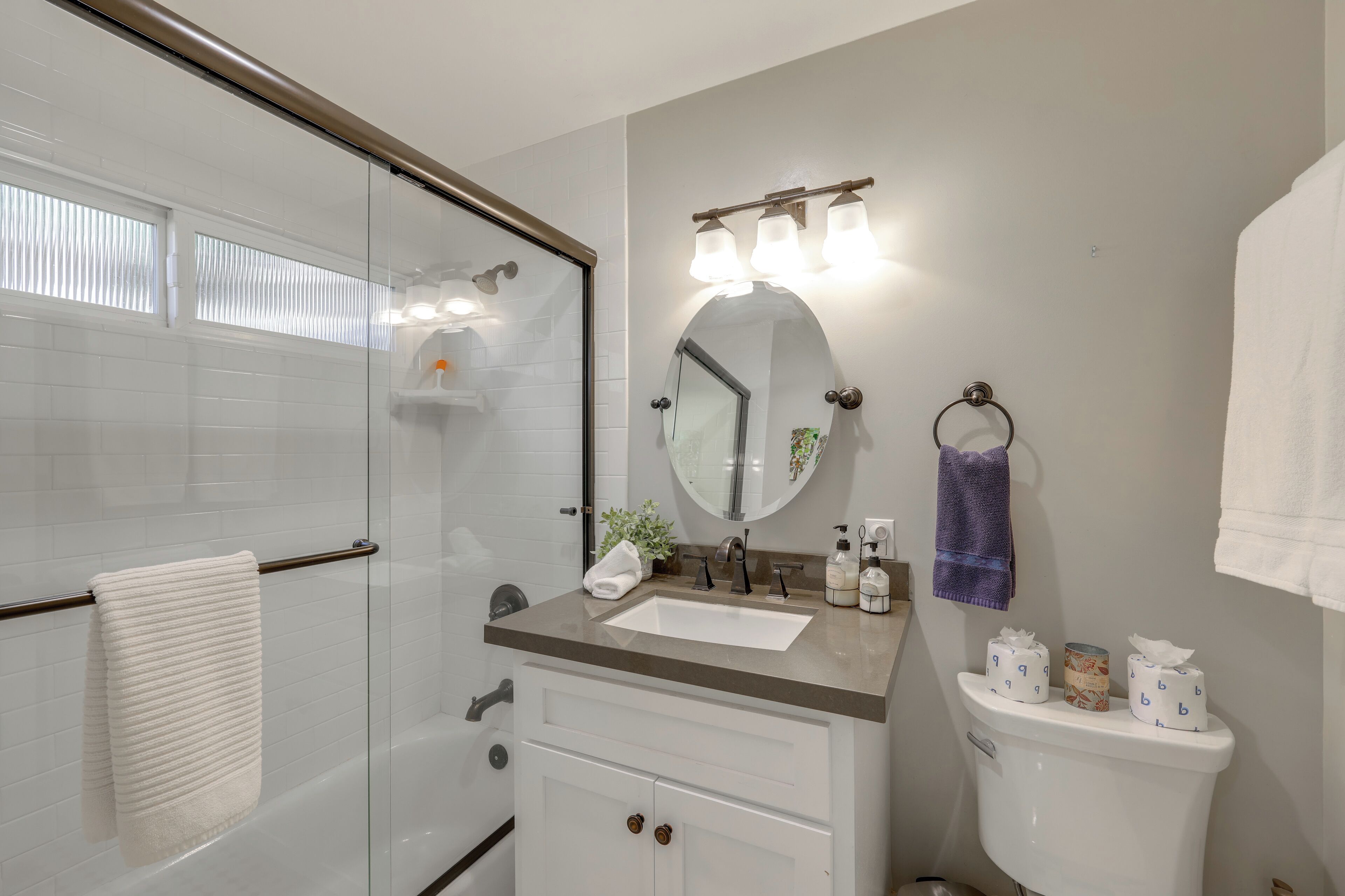 A bathroom with a glass shower enclosure, a sink with a vanity, a toilet, and a mirror with lights.