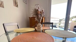 A dining table with glass top and woven placemats, a vase with dried flowers, and a view of a balcony with a railing. - Le Cocon Provençal, T2 Downtown Hyères (Hyères)